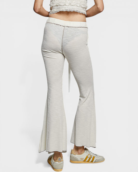 Person wearing light gray flared pants with a white top on a white background