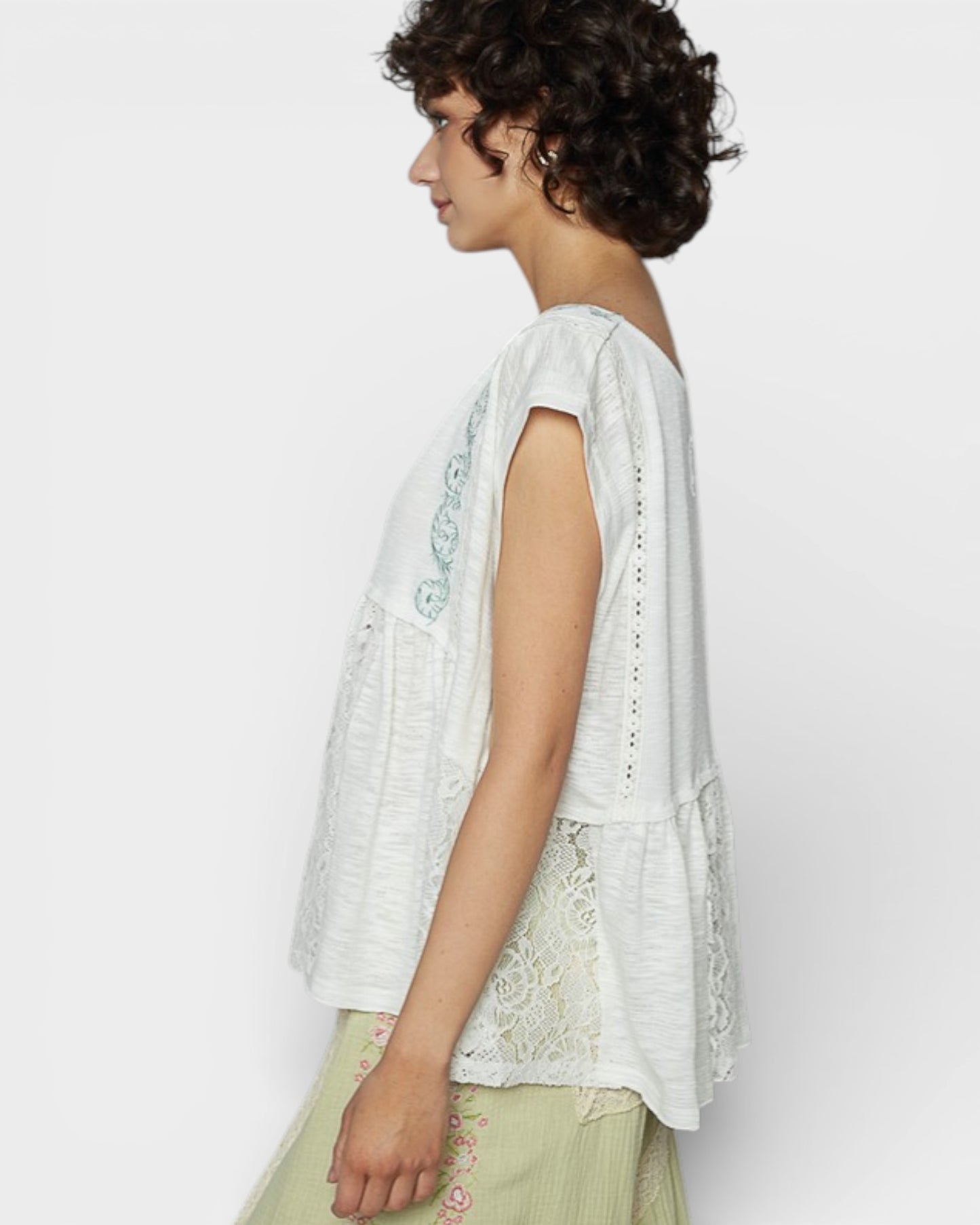 Woman wearing a light-colored embroidered top and skirt against a white background