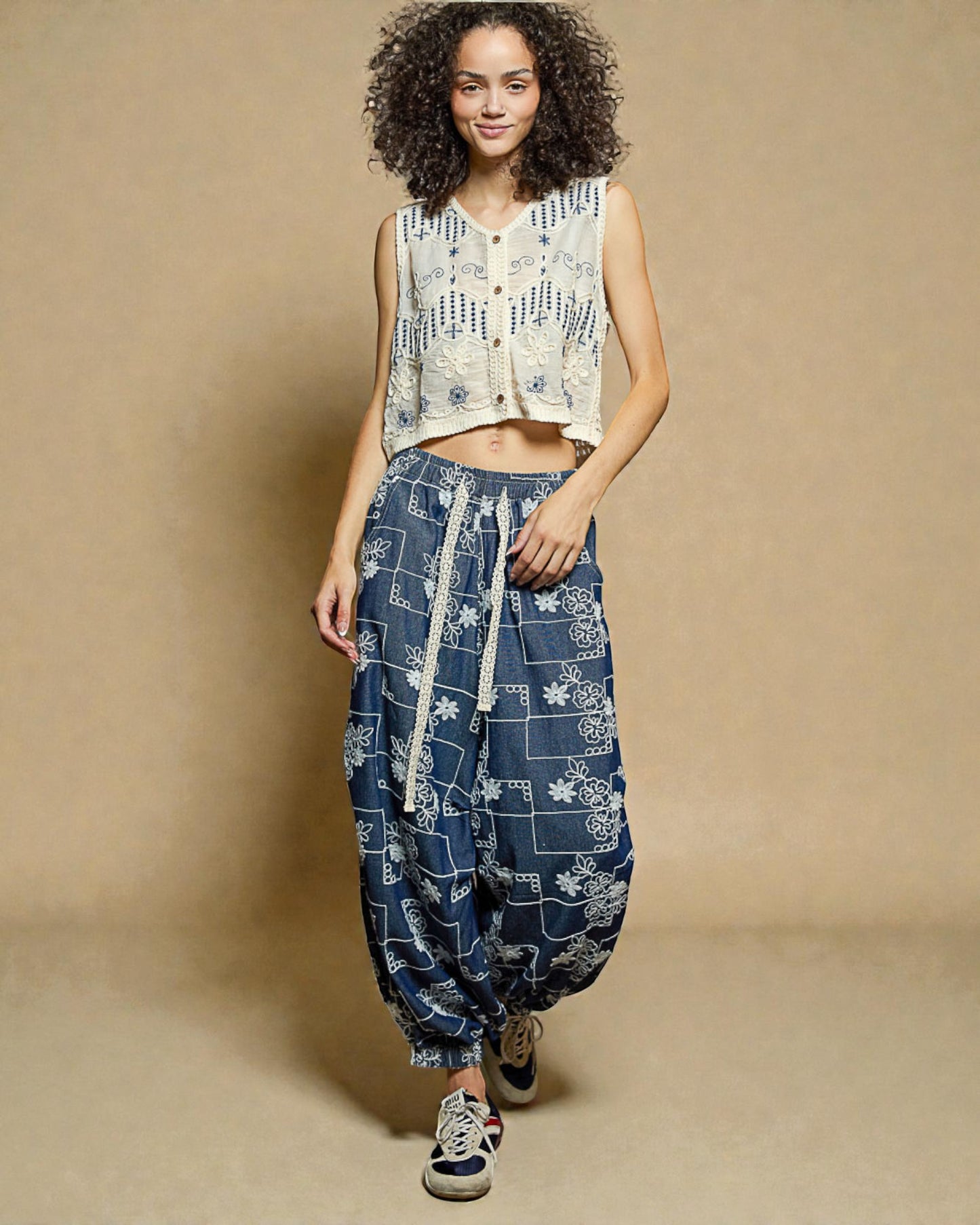 Woman wearing a sleeveless top and patterned harem pants on a beige background