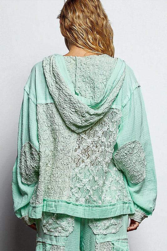 Person wearing a light green lace outfit with a hood on a plain background