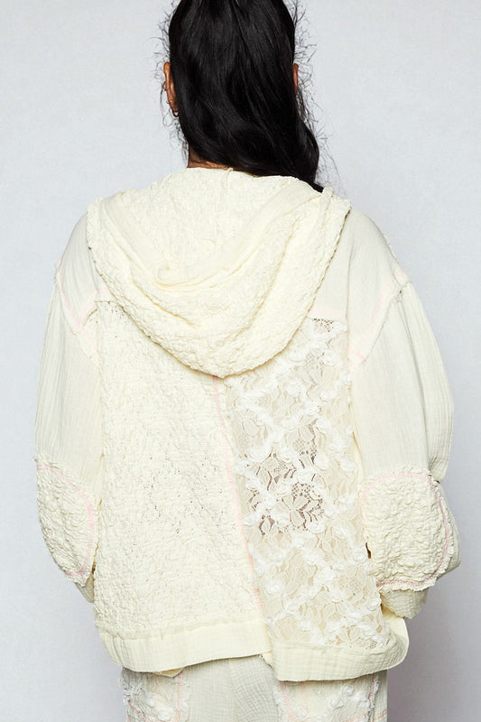 Person wearing a textured cream-colored hoodie with floral lace details on a plain background