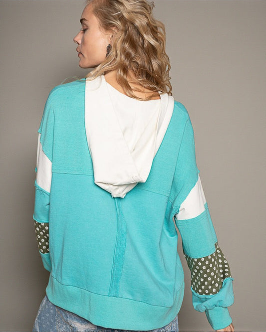 Person wearing a turquoise and white hoodie with polka dot sleeves on a plain background