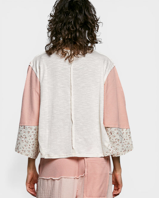 Person wearing a light-colored top with pink sleeves and floral cuffs on a white background