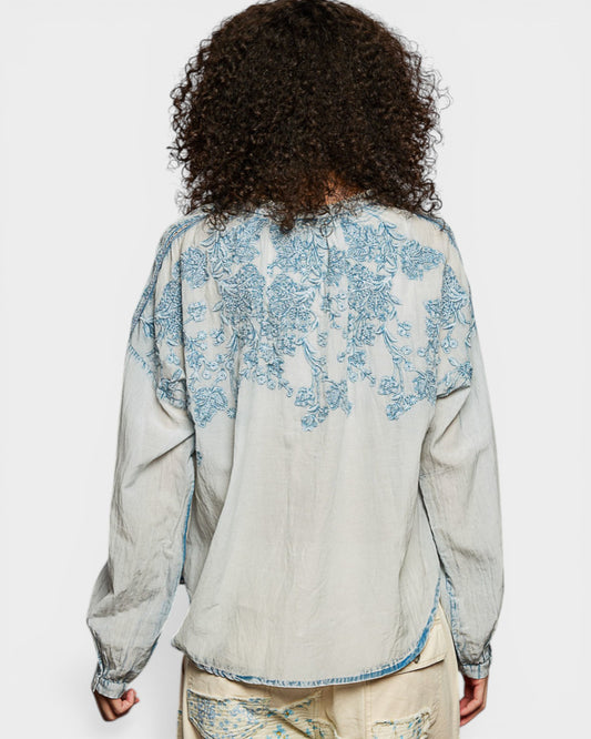 Person wearing a light-colored shirt with blue floral patterns on a white background