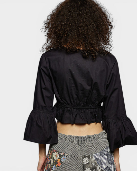 Person wearing a black bell-sleeve top with a plain background