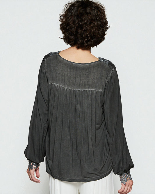 Person wearing a dark gray blouse with floral embellishments on a white background