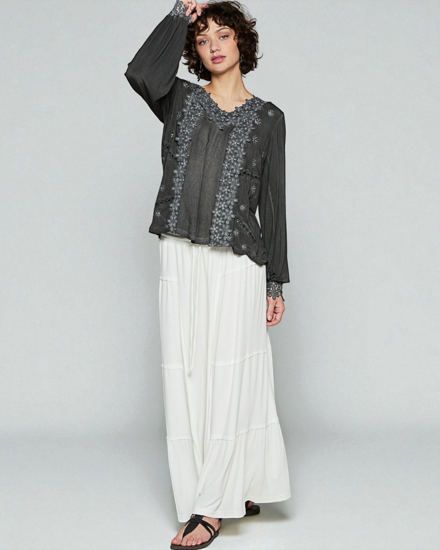 Woman wearing a black floral top and white pants on a gray background