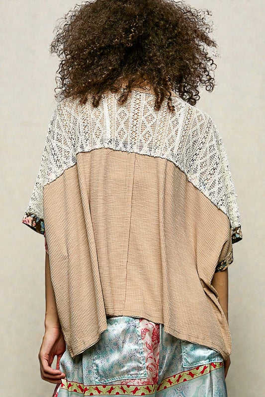 Person wearing a beige and white top with a textured pattern, standing against a plain background