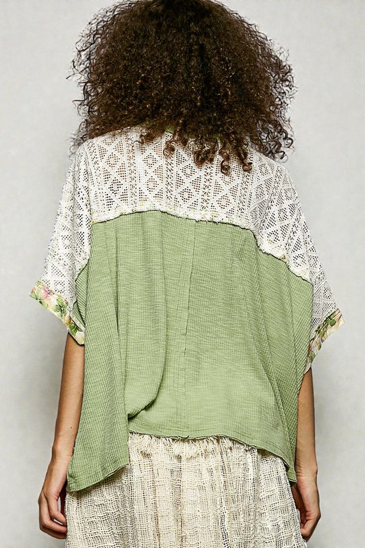 Person wearing a green top with lace details on a plain background