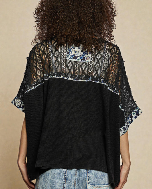 Person wearing a black top with floral lace details on a beige background