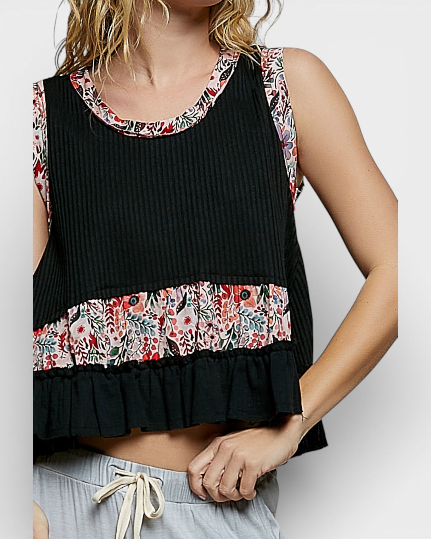 Black sleeveless top with floral trim worn by a person on a white background