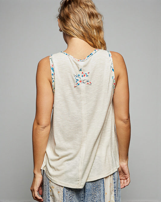 Person wearing a beige sleeveless top with floral patterns on a gray background