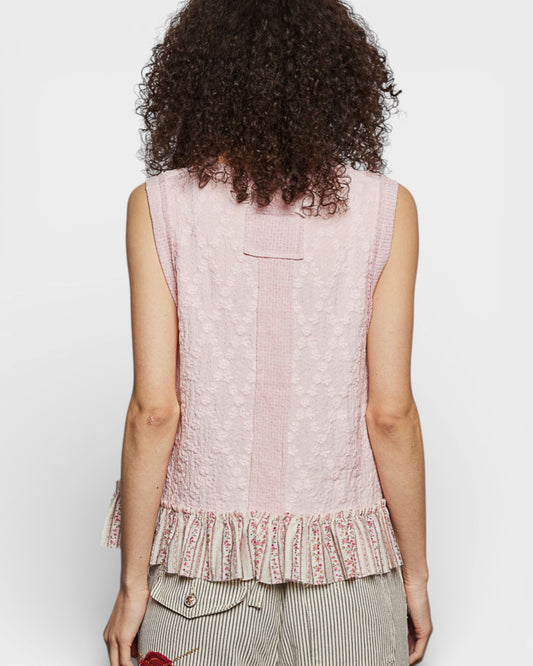 Person wearing a light pink sleeveless top with ruffled hem on a white background
