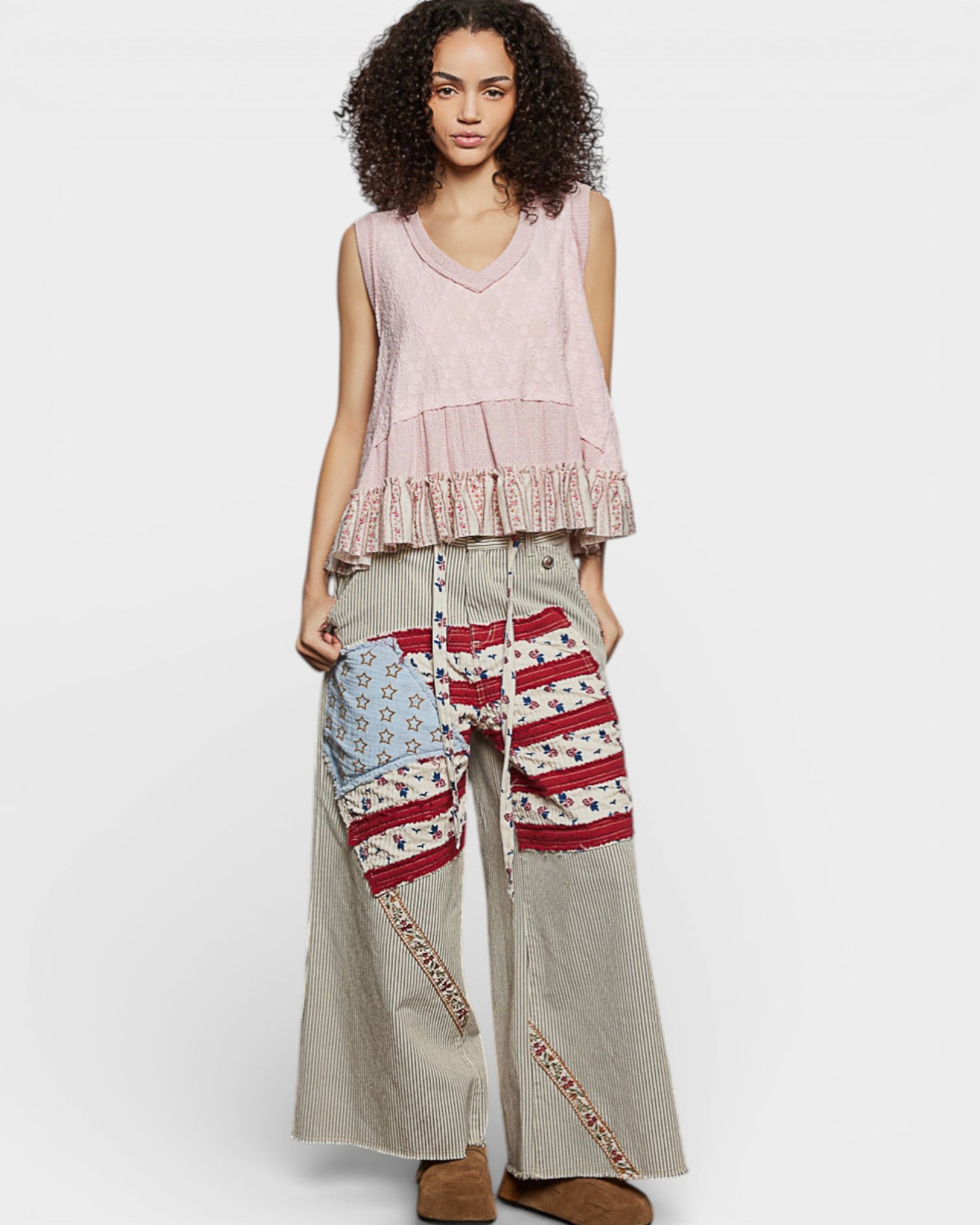 Woman wearing a sleeveless pink top and wide-leg pants with American flag pattern on a white background