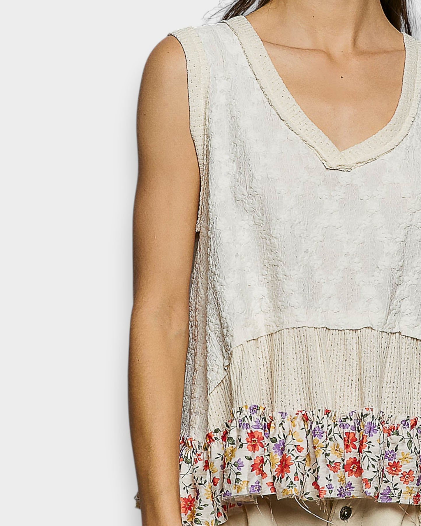 Light-colored sleeveless top with floral hem on a white background