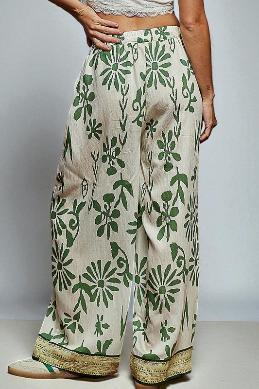 Beige pants with green floral pattern worn by a person on a plain background