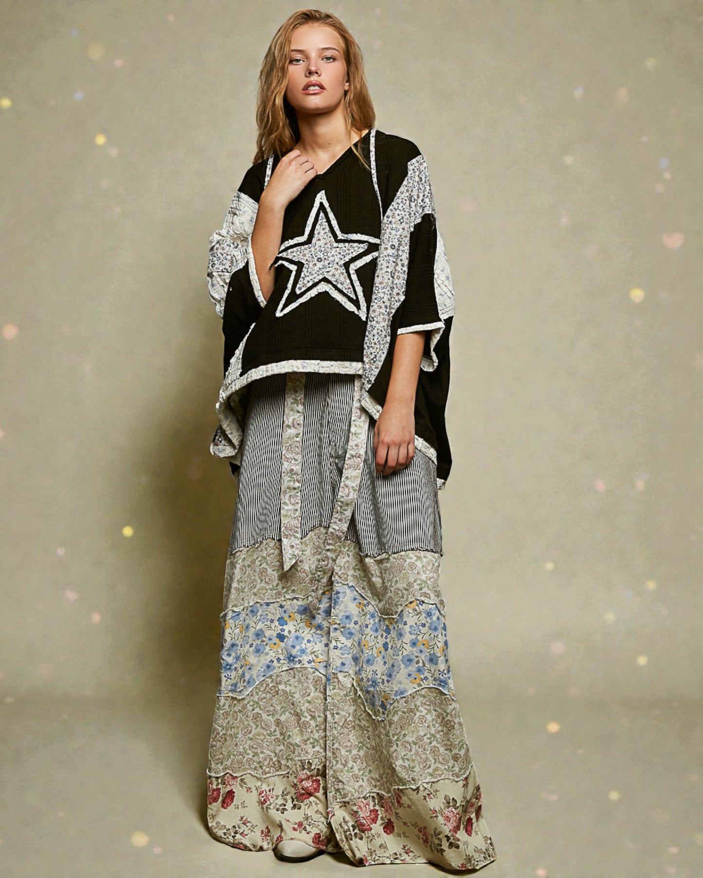 Woman wearing a black and white star-patterned top with a long, patchwork skirt on a beige background.