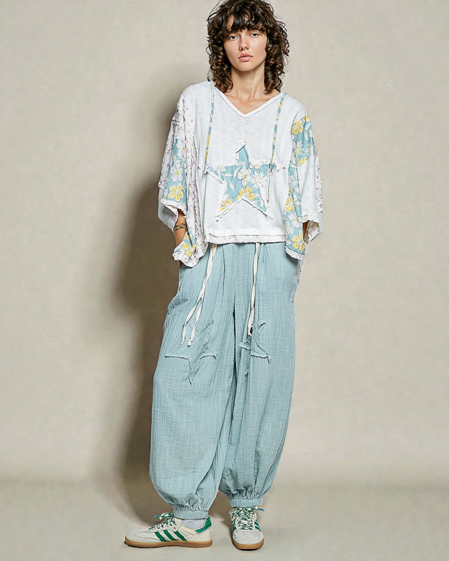 Person wearing a floral kimono, white shirt with star design, light blue pants, and green sneakers on a plain background