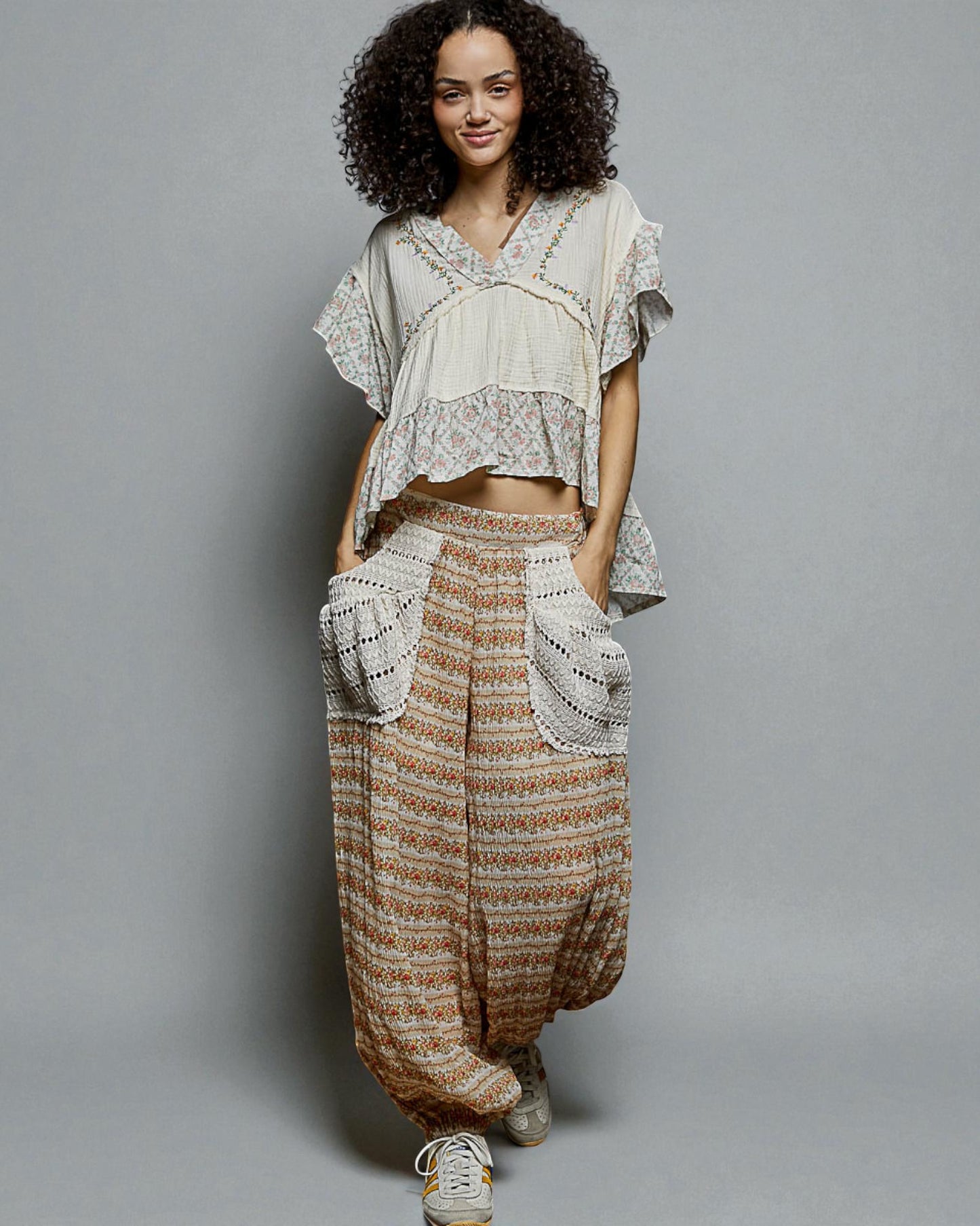 Woman wearing a bohemian outfit with a white top and patterned pants on a gray background