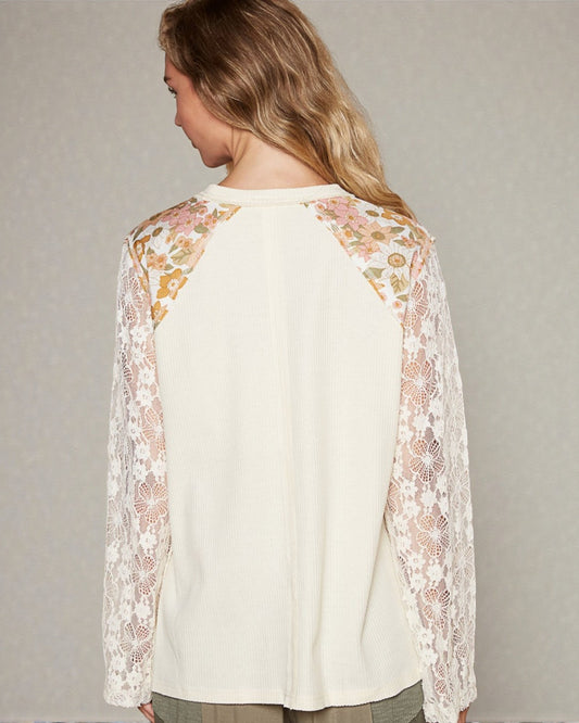 Woman wearing a cream-colored top with floral lace sleeves against a neutral background