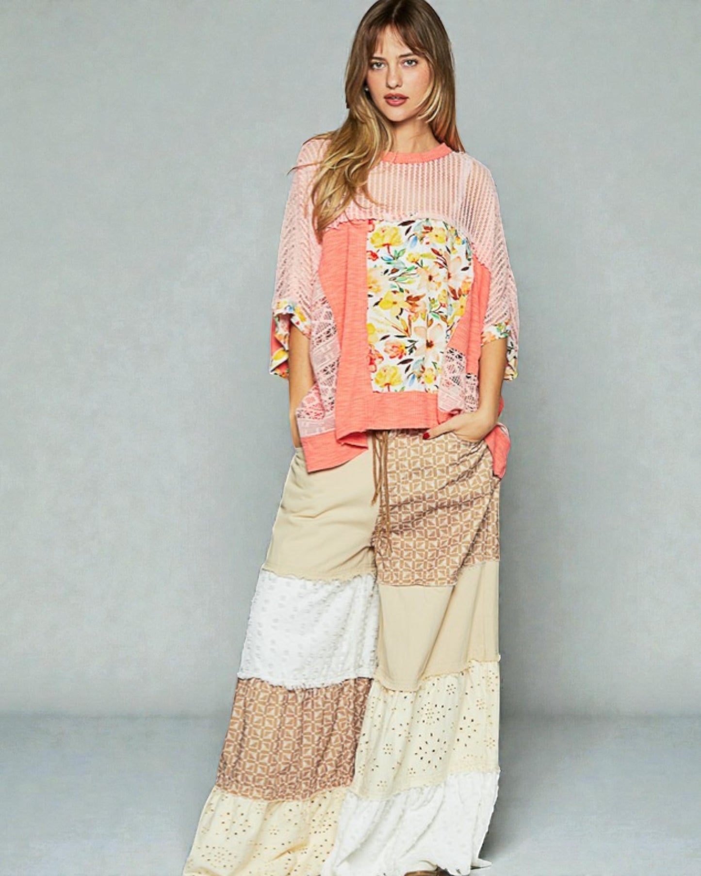 Woman wearing a colorful outfit with a floral top and patterned pants on a gray background