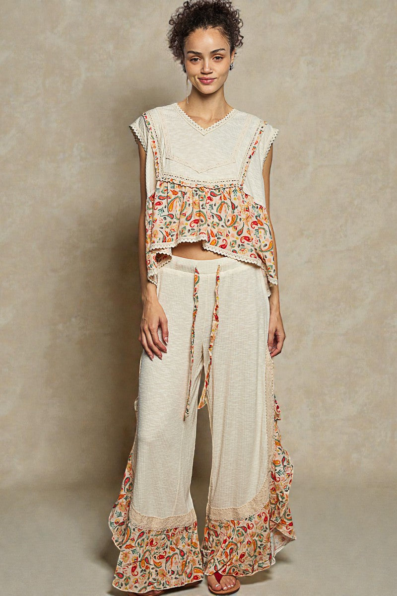 Woman wearing a floral top and white pants with a beige background