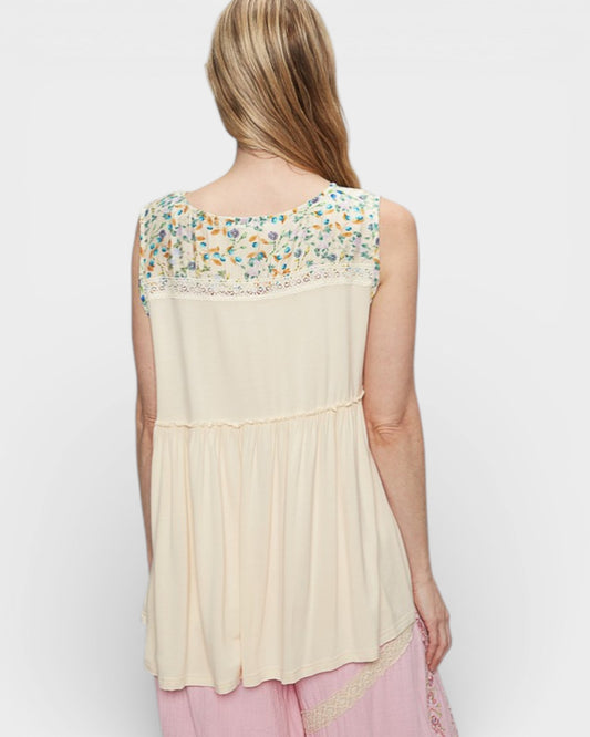 Woman wearing a sleeveless top with floral lace details on a plain background