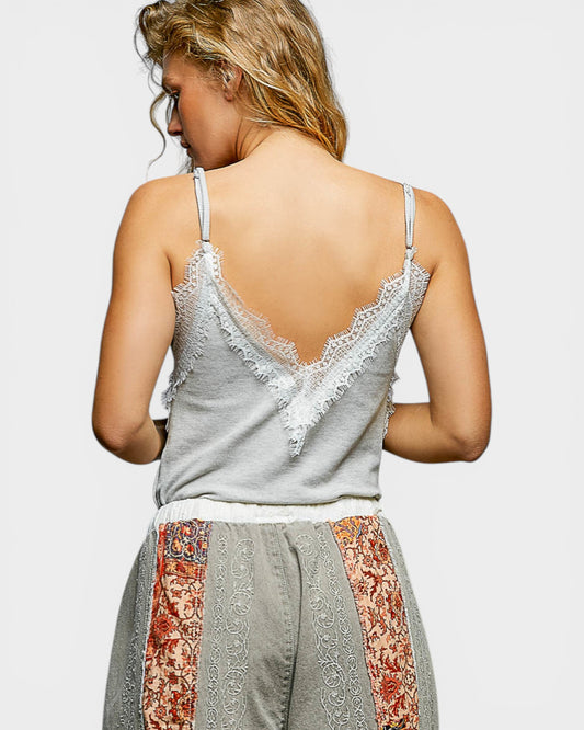 Woman wearing a gray lace-trimmed top with floral pants on a plain background