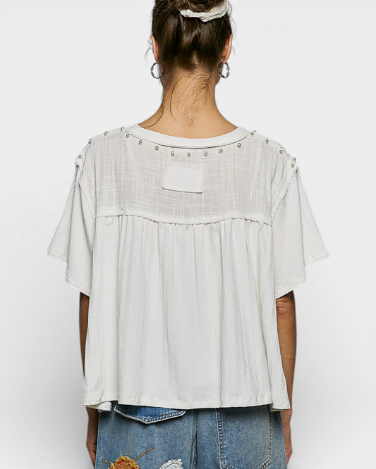 Person wearing a white blouse with embellishments on a plain background