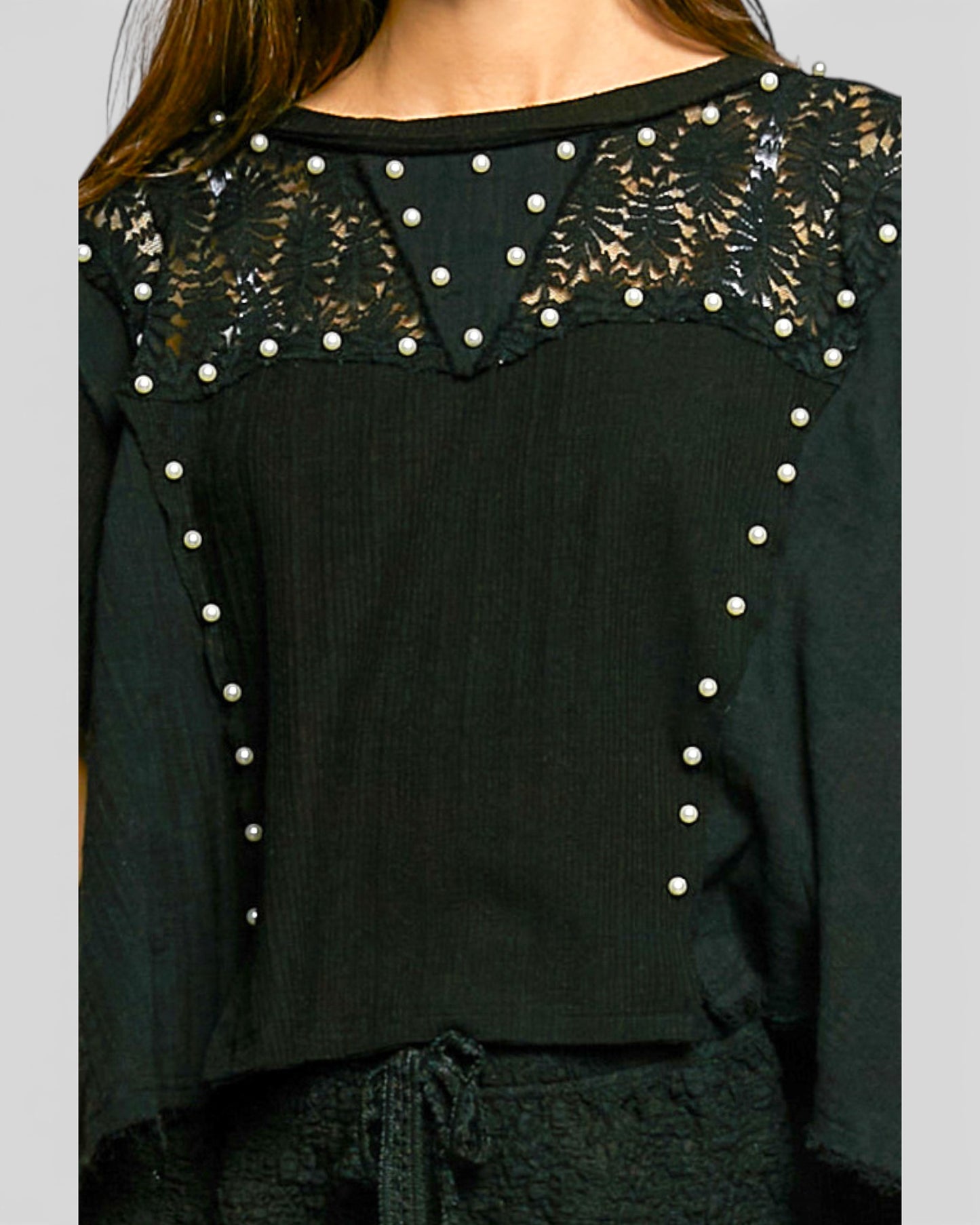 Black top with lace and pearl details on a plain background