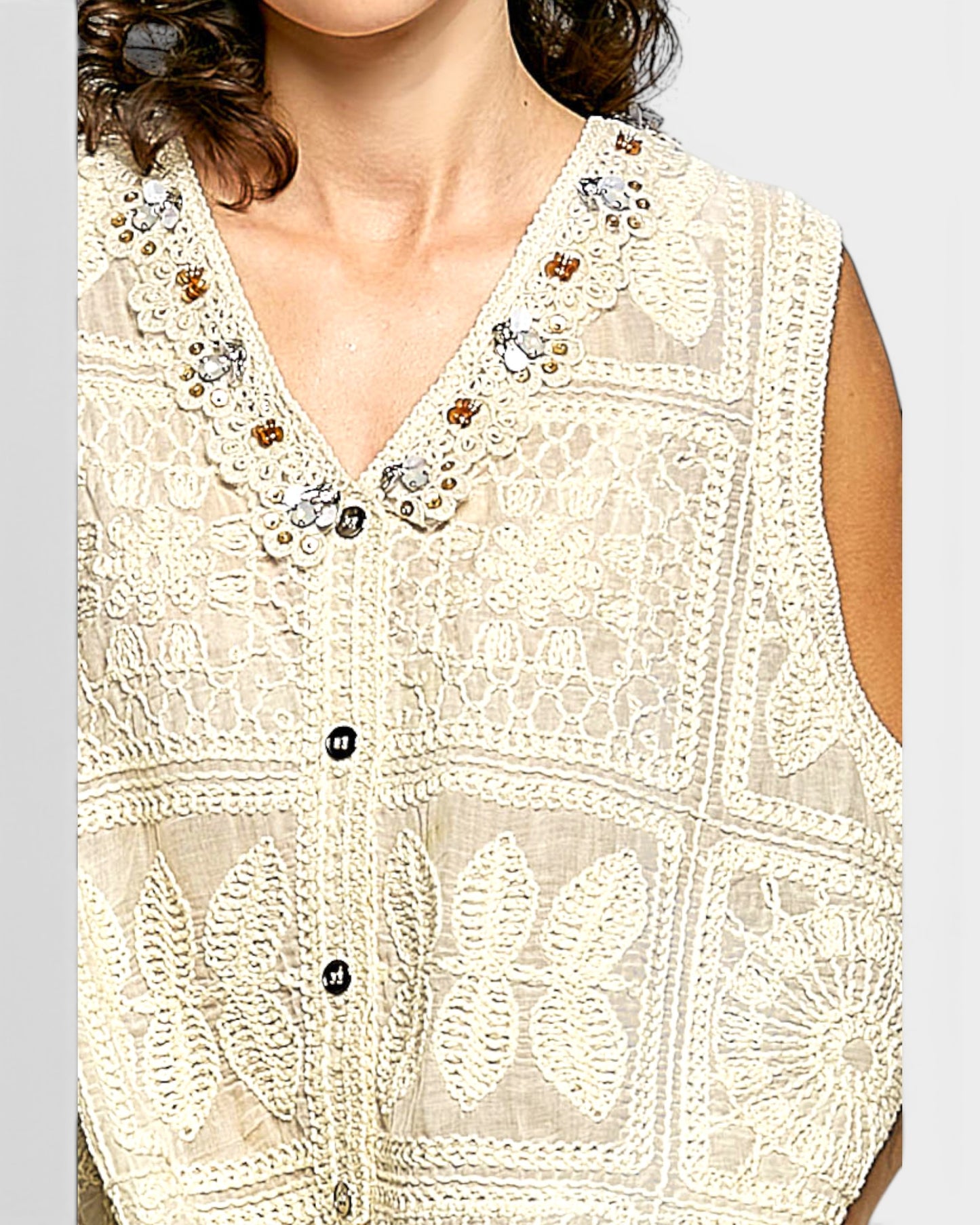 Close-up of a beige embroidered vest with buttons on a plain background