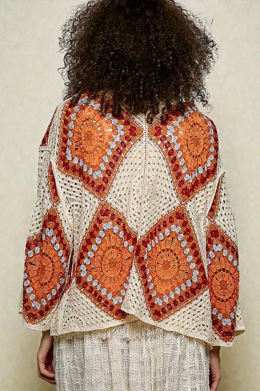 Person wearing a crocheted orange and beige patterned shawl on a neutral background