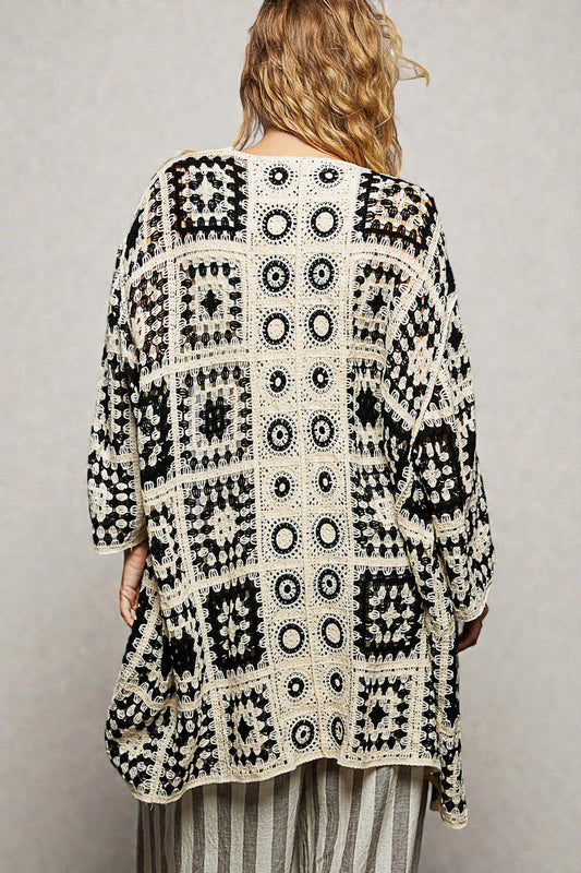 Person wearing a black and white patterned crochet cardigan against a plain background