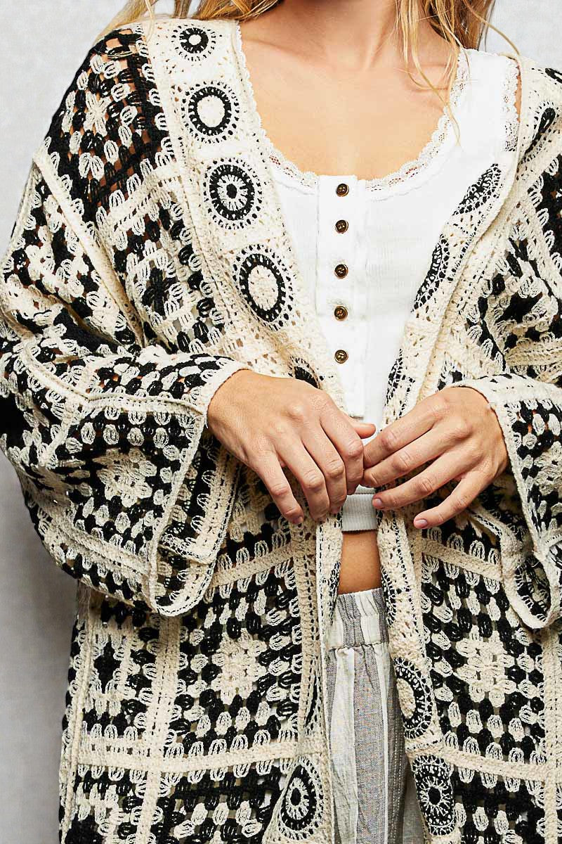 Person wearing a black and white patterned cardigan over a white shirt.