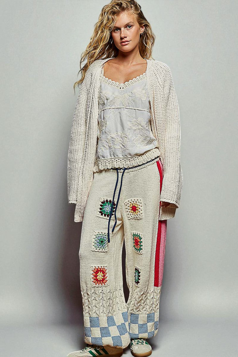 Woman wearing a stylish outfit with a patterned cardigan, top, and pants on a plain background