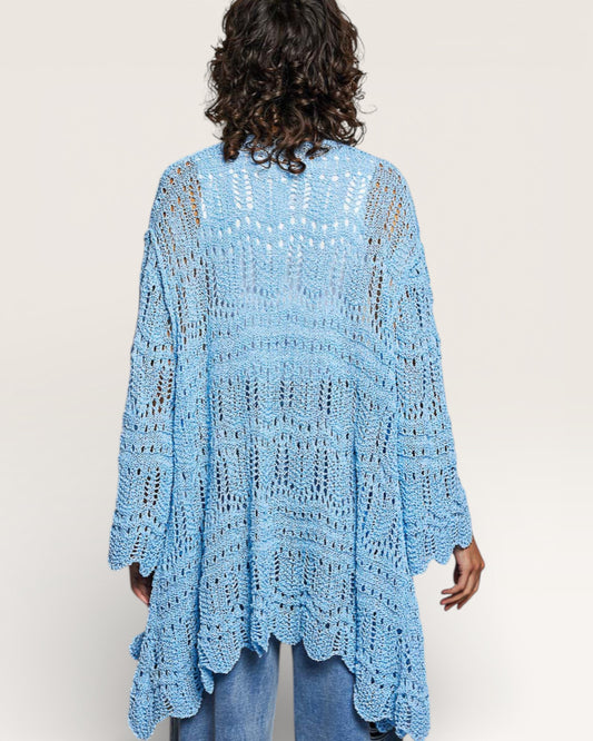 Person wearing a light blue crocheted poncho against a plain background