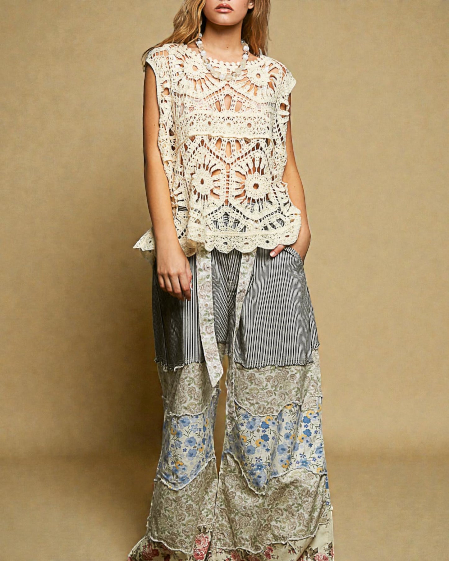 Woman wearing a floral and lace top with layered, patterned pants against a beige background