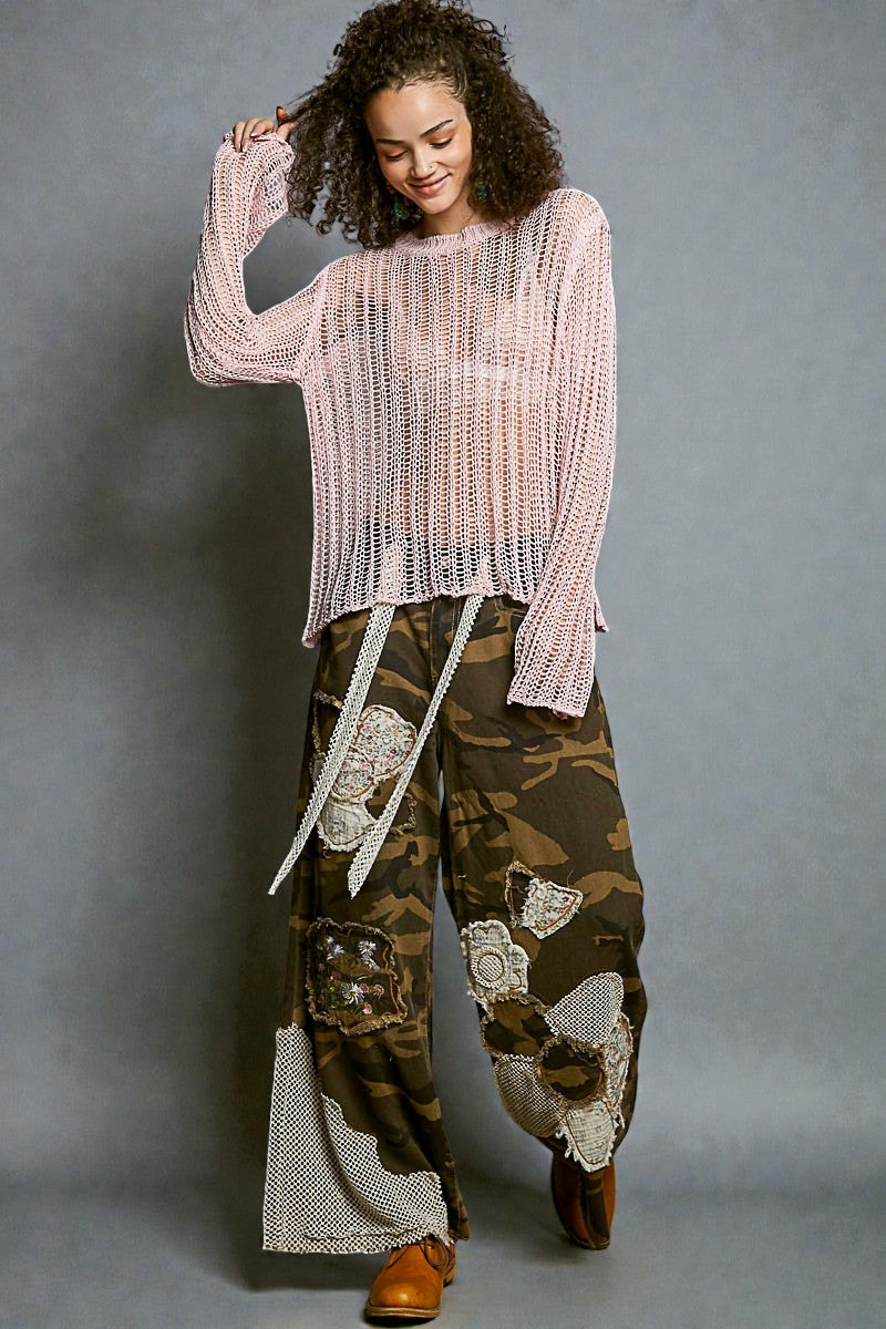 Woman wearing a pink knit top and camouflage pants with white patterns on a gray background