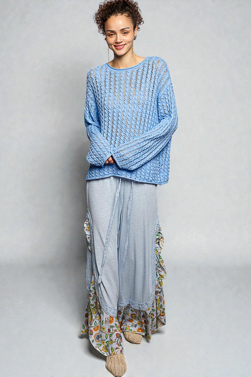 Woman wearing a blue knitted sweater and light-colored skirt with floral patterns on a plain background