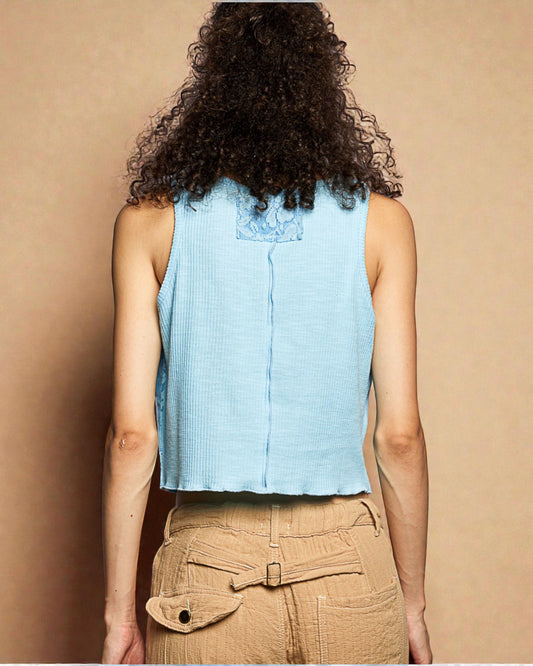 Person wearing a light blue sleeveless top and beige pants against a beige background