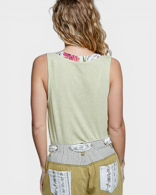 Person wearing a sleeveless green top with floral pattern on the neckline, beige pants with white embroidery, and a belt.