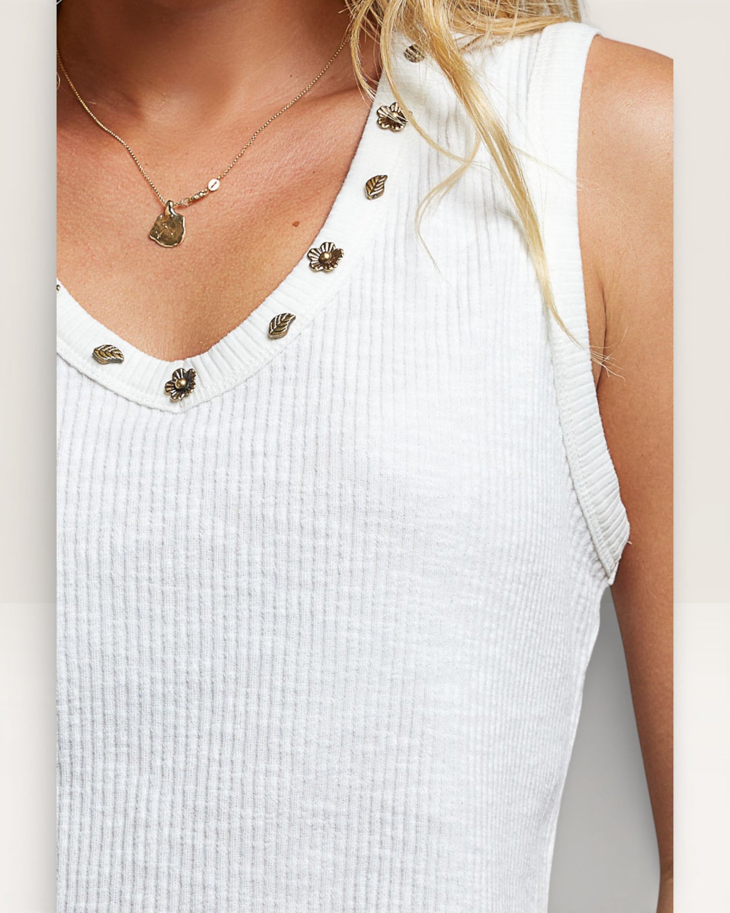 White sleeveless top with decorative buttons on a plain background