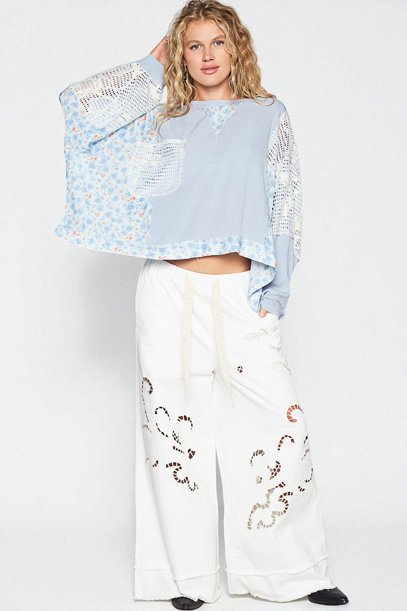 Woman wearing a light blue embroidered top and white pants with embroidery on a white background