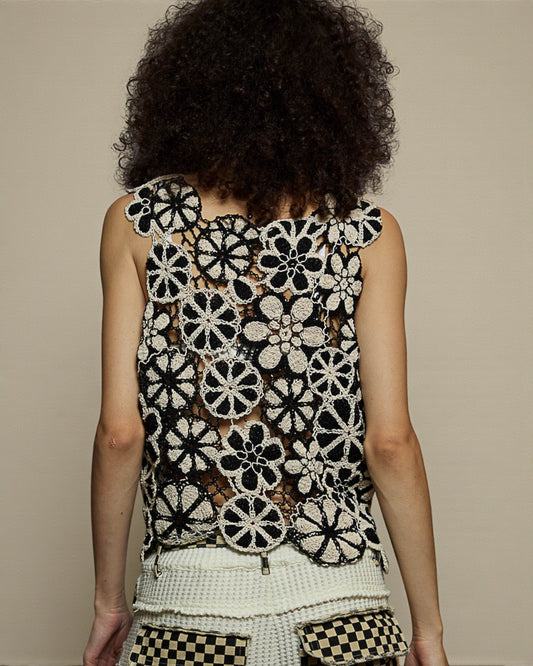 Person wearing a black and white floral crochet top against a beige background