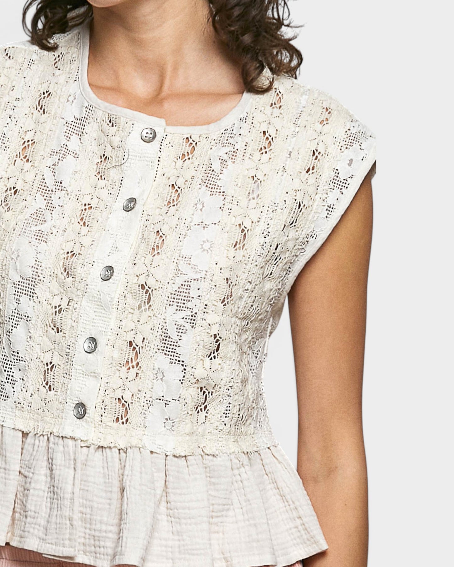 Close-up of a woman wearing a white lace top with buttons on a plain background