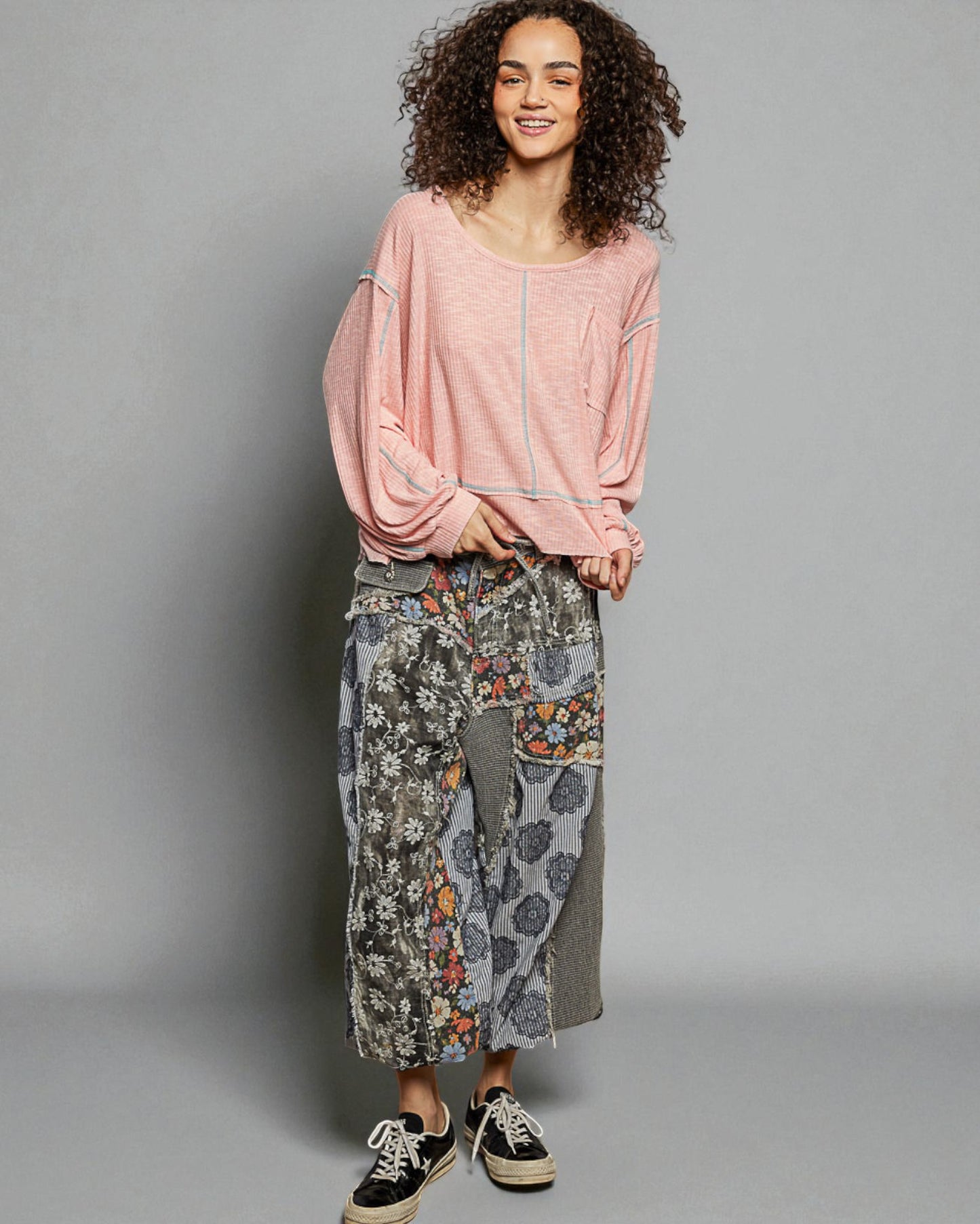 Woman wearing a pink top and patterned pants on a gray background