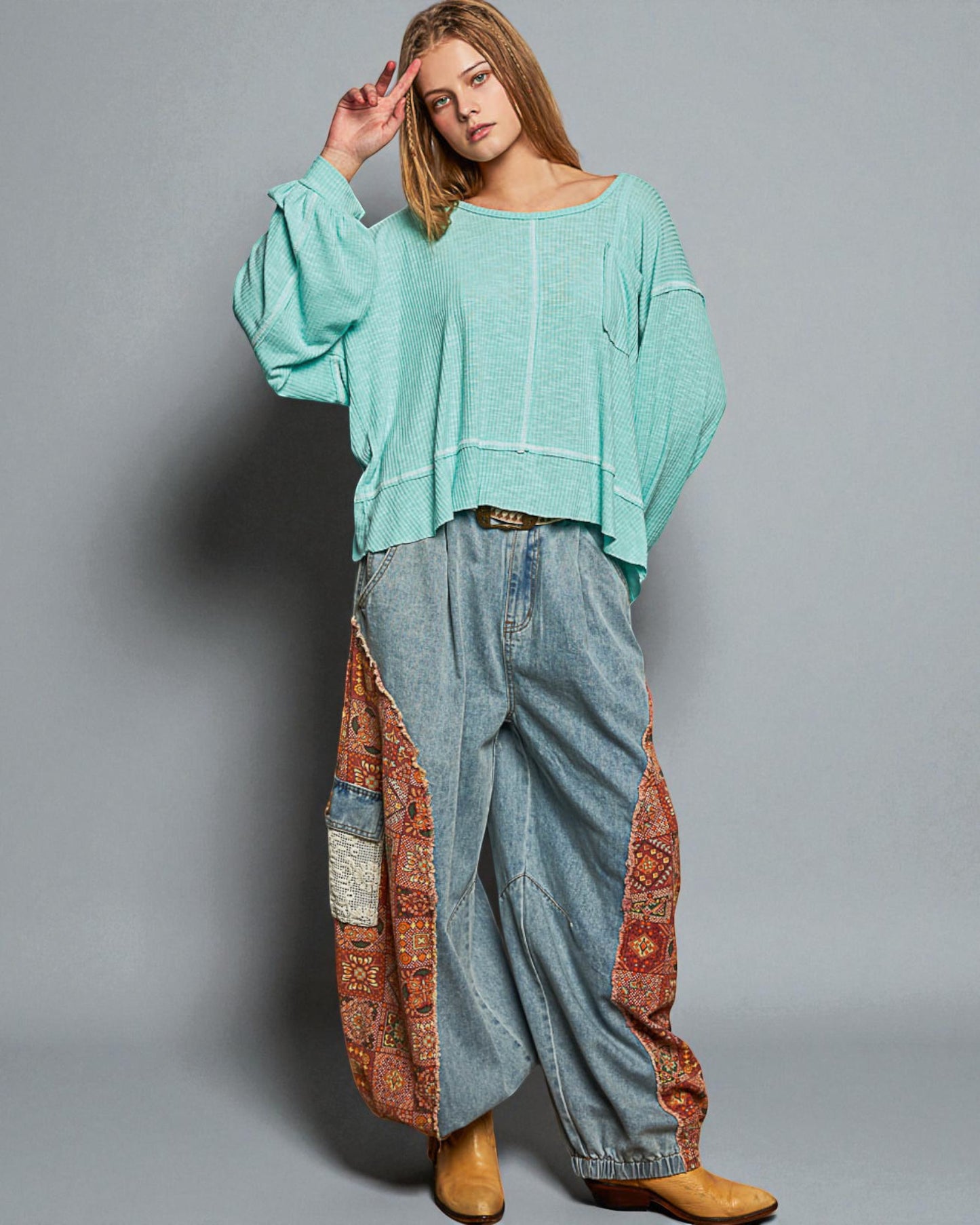 Person wearing a teal sweater and patterned pants on a gray background