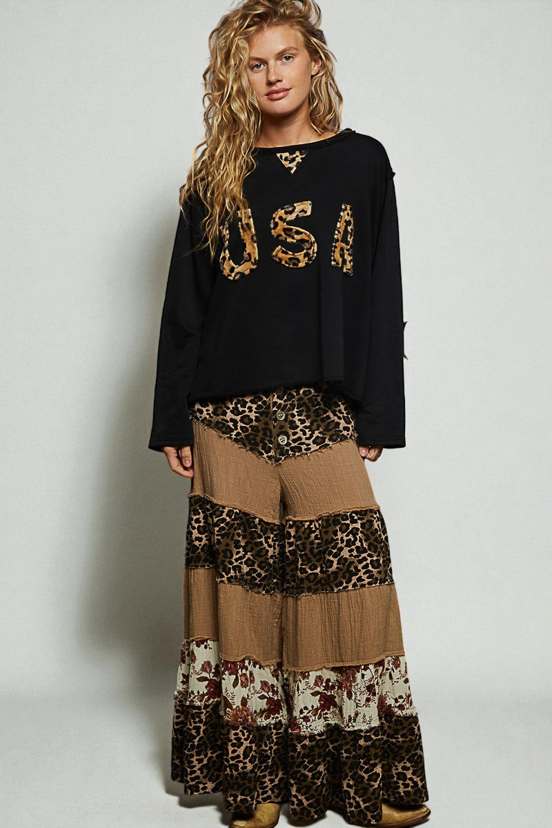 Woman wearing a black 'USA' sweatshirt and patterned pants on a plain background
