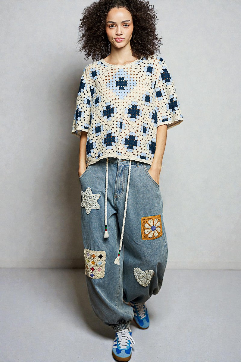 Person wearing a patterned top and patchwork jeans against a plain background