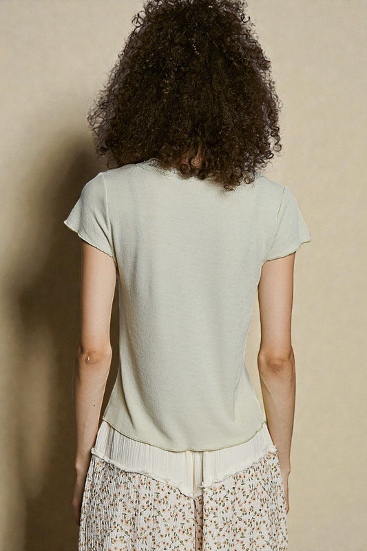 Person wearing a light green t-shirt and floral pants against a beige background